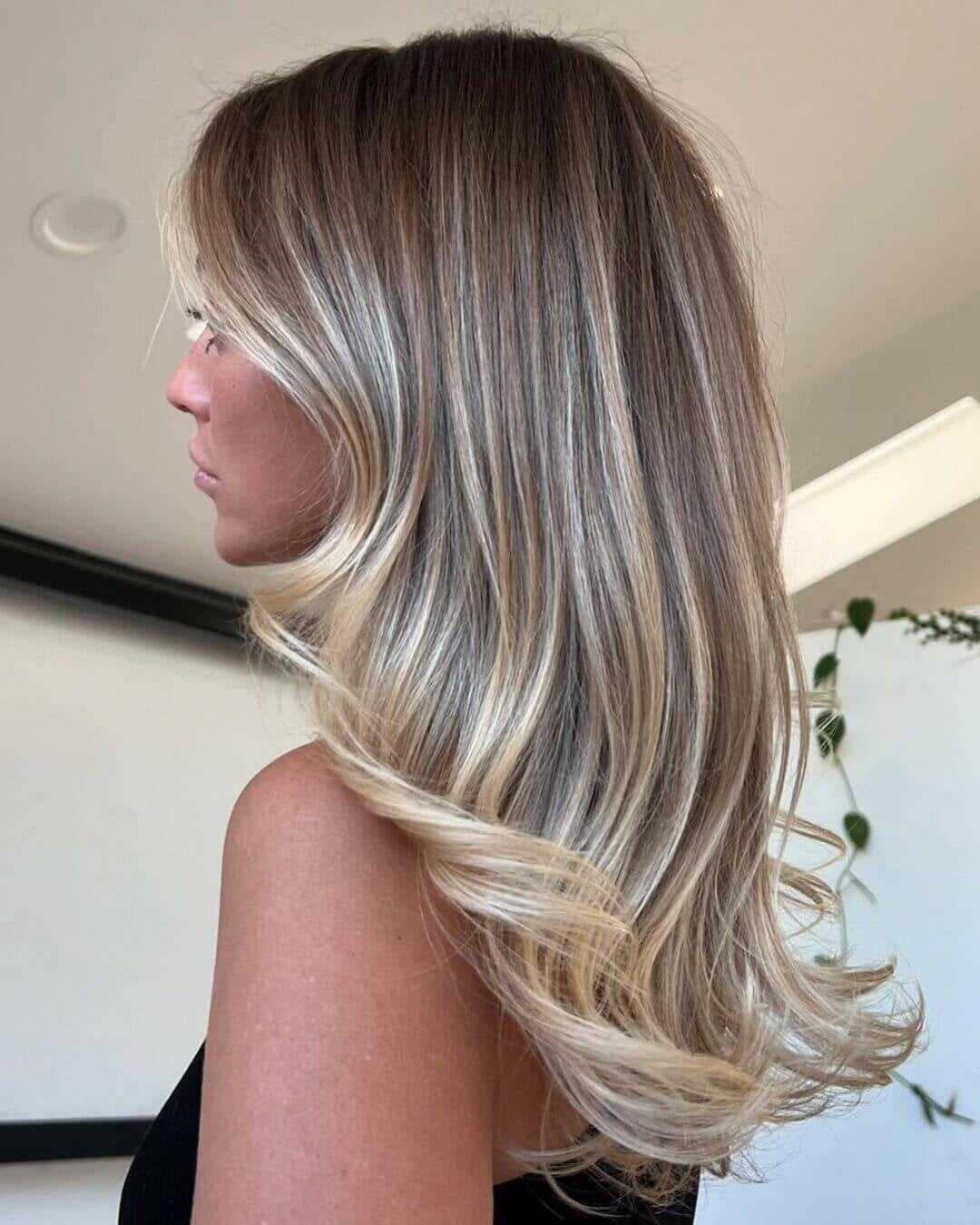 Blonde woman with wavy, layered hair in a stylish indoor setting.