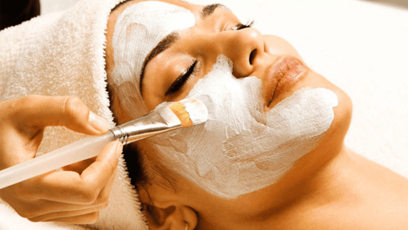 Person receiving a facial treatment with a brush applying a white mask.