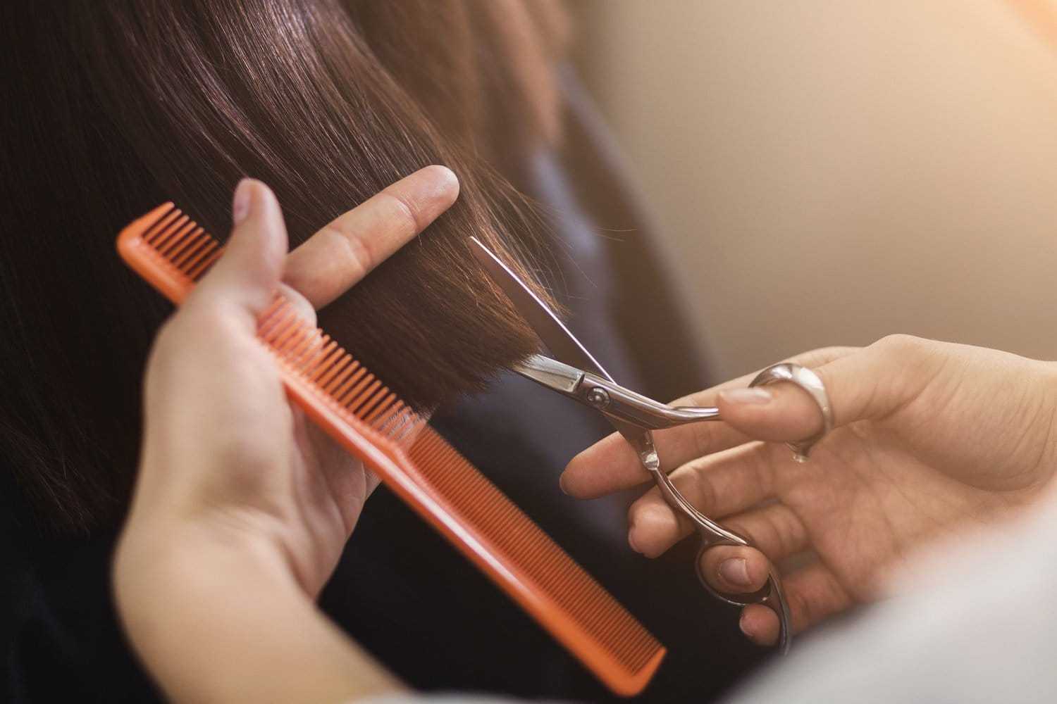 Hairdresser cutting brown hair with scissors and an orange comb.