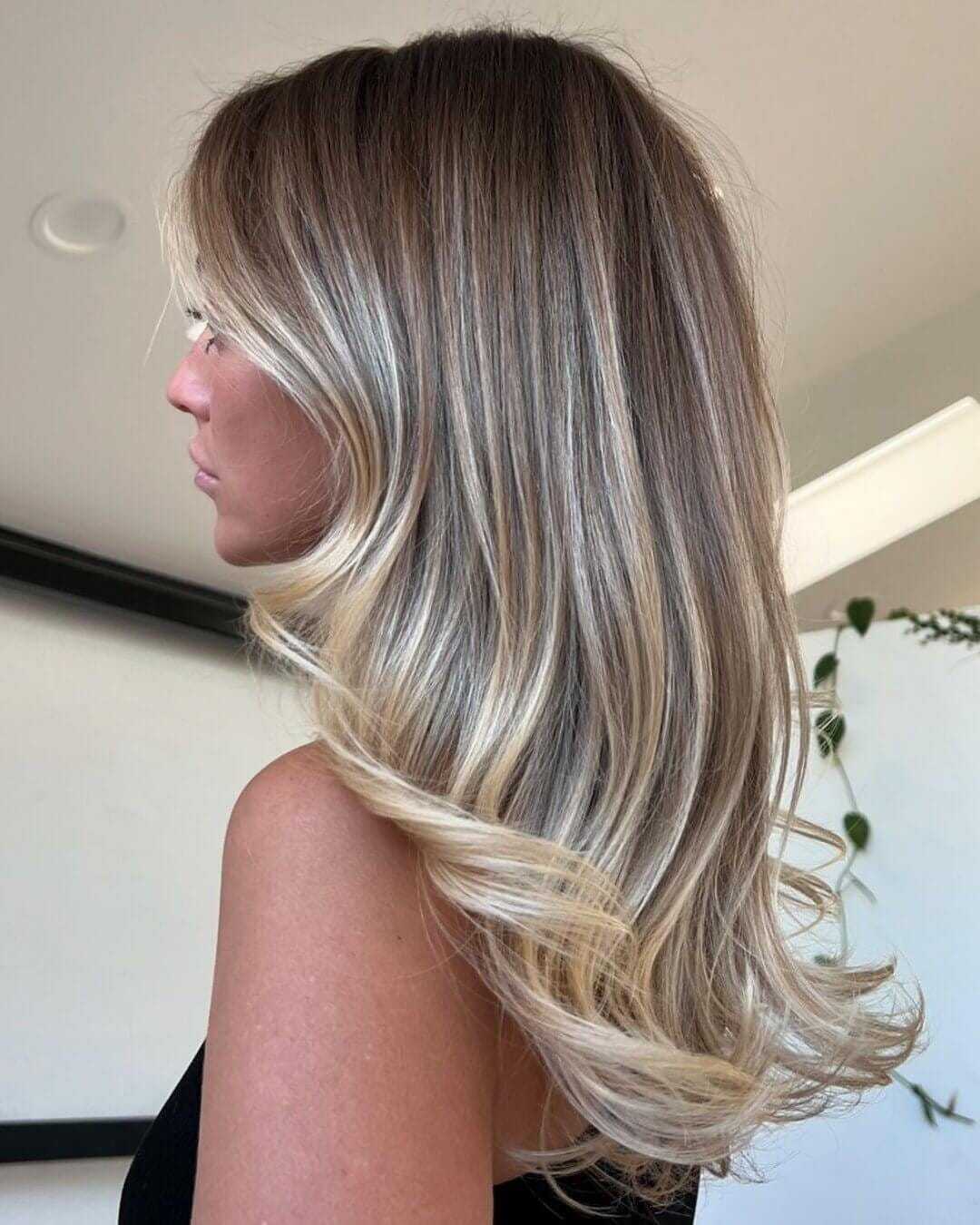 Blonde woman with wavy, layered hair in a stylish indoor setting.
